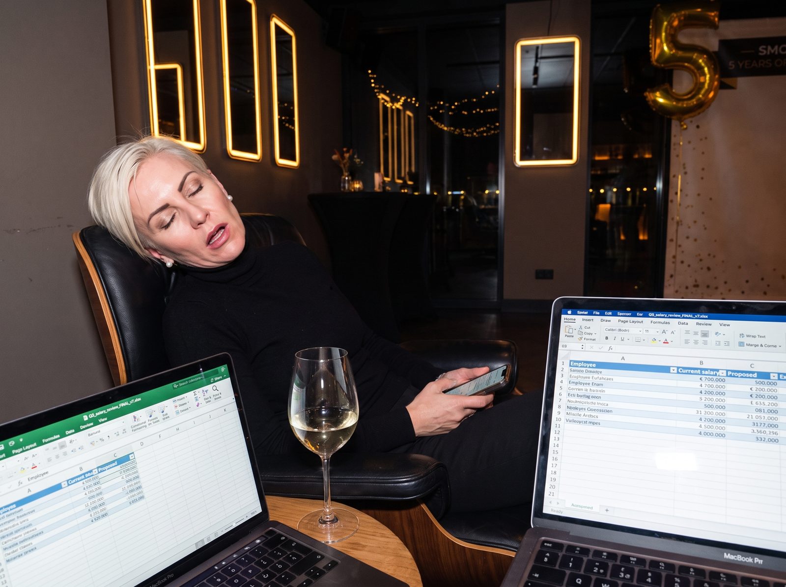 Mireille asleep in a lounge chair next to an open laptop showing a salary spreadsheet.